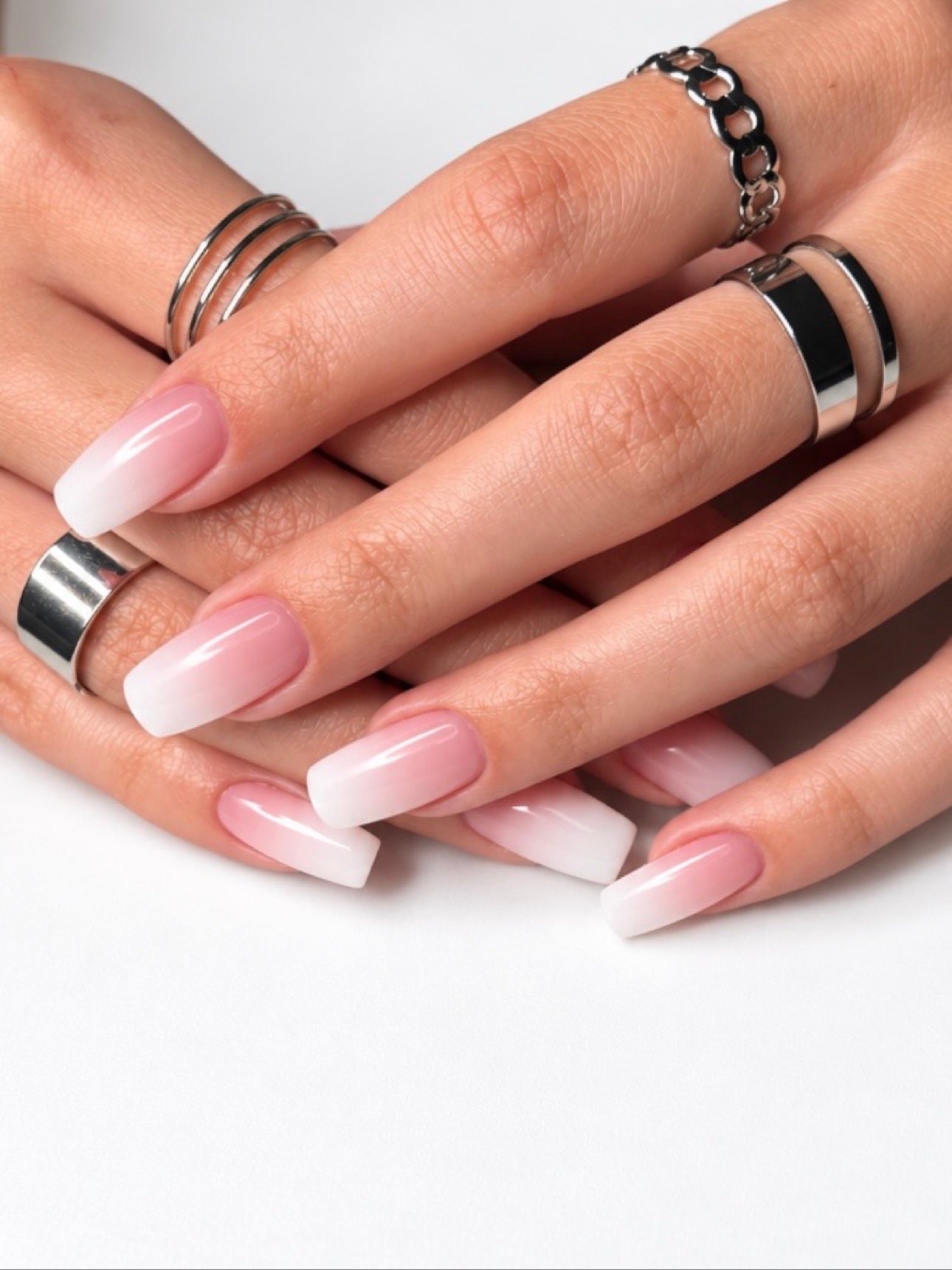 Close-up of hands with a pink-and-white ombre manicure and silver rings